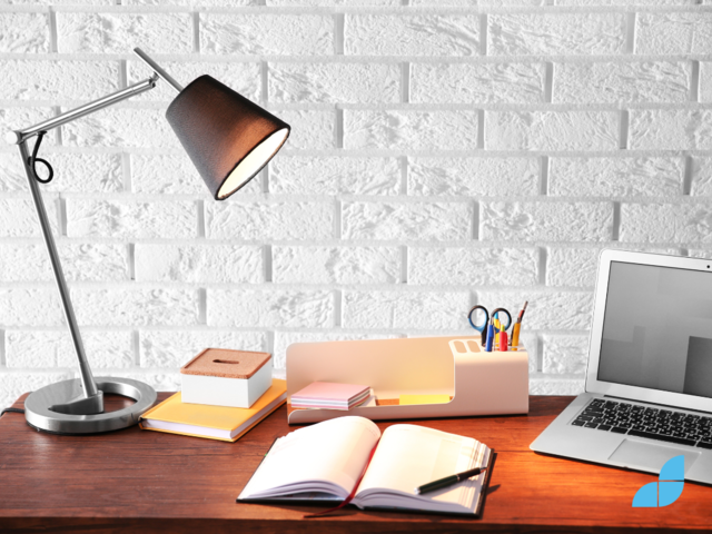 A desk with a desk lamp, notepad, laptop and desk accessories/organisers. 